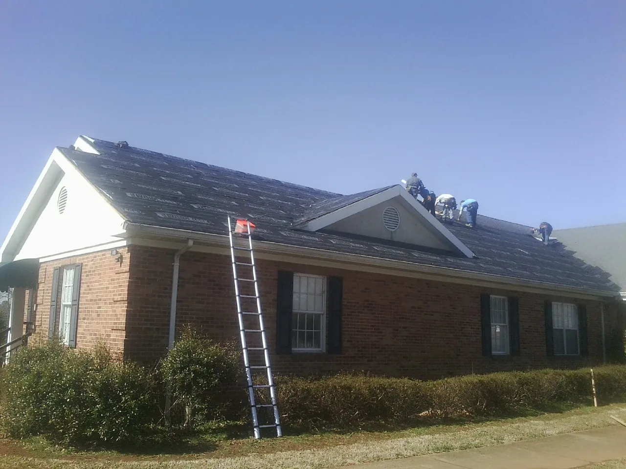 Crew tearing shingles off a brick ranch roof with a ladder set — Metal Roof Repair work by our crew in Kuna