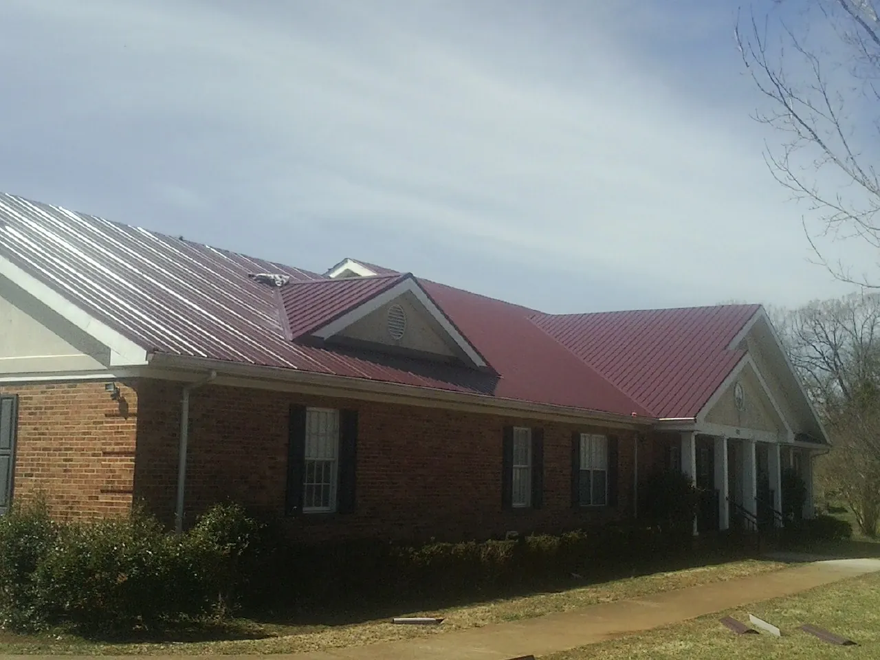 Red metal roof with gabled entries on a long brick building, from a Hail Damage Roof Repair job in Kuna