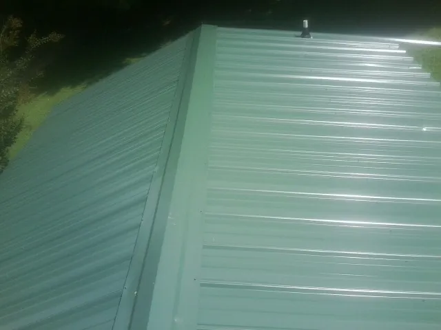 New green metal panels meeting at the ridge of a roof — Flat Roof Repair work by our crew in Kuna