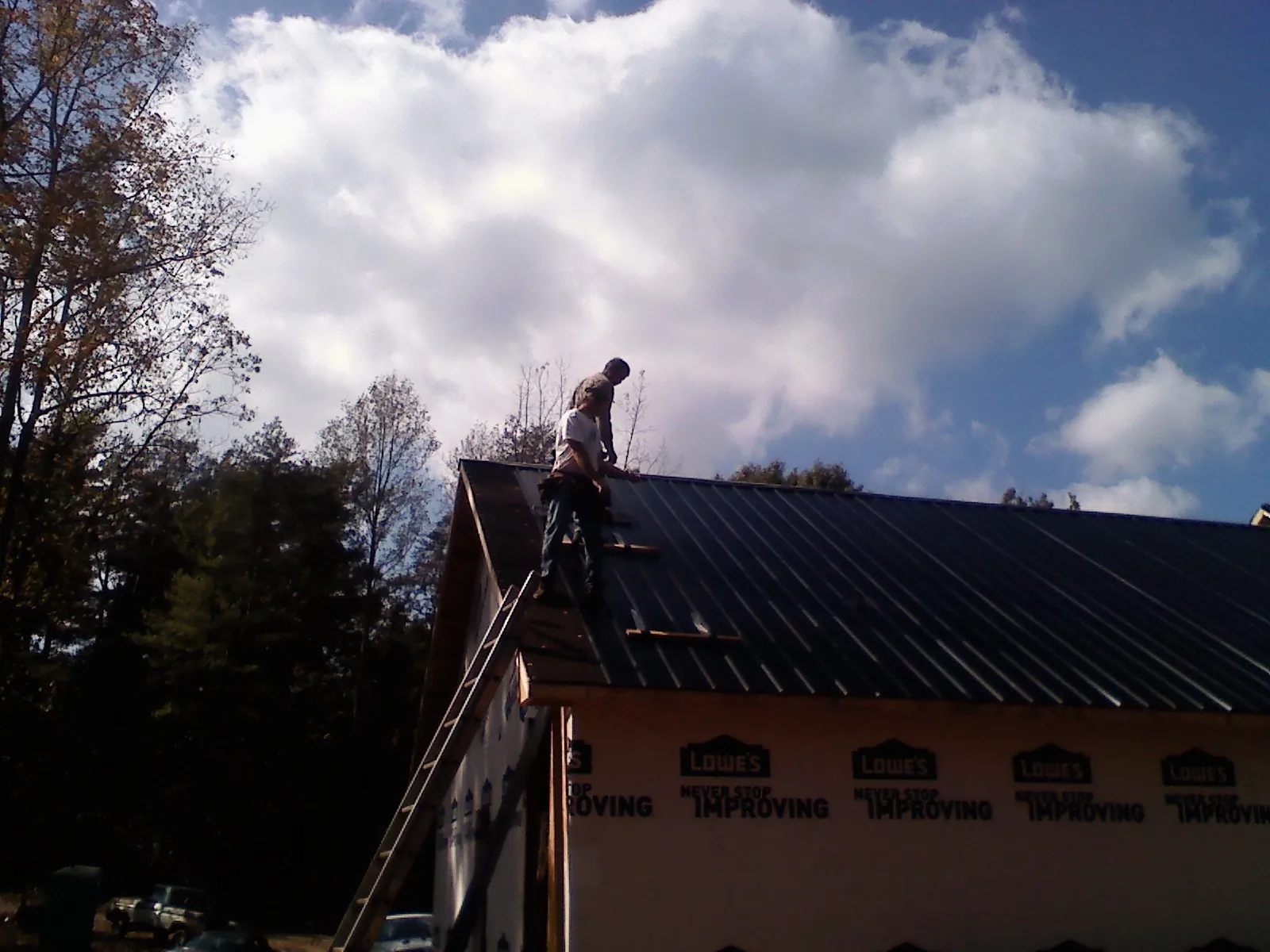 Roofer fastening dark metal panels high against a cloudy sky, from a Roof Inspection job in Kuna