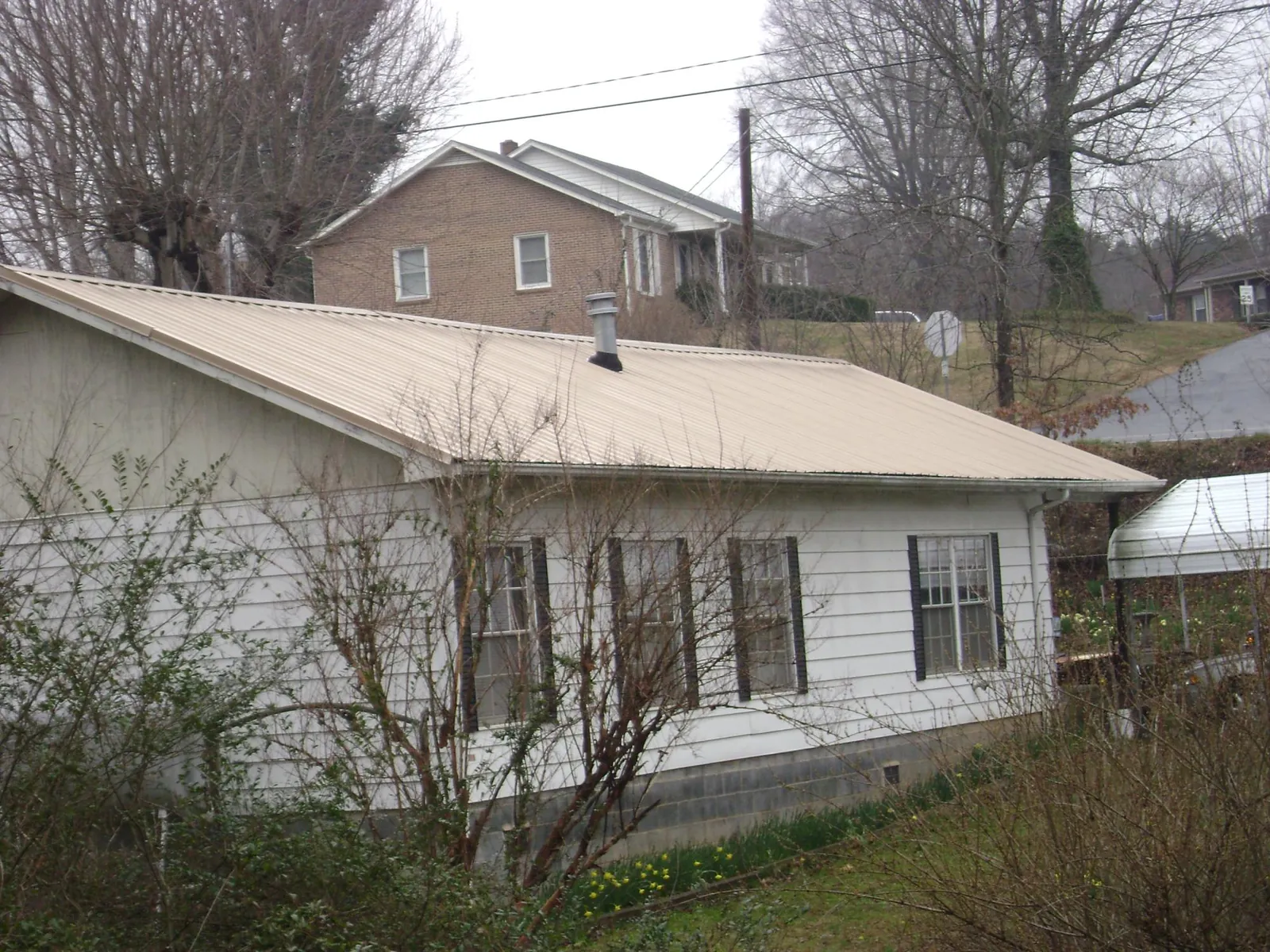 Tan metal roof on a white sided house set into a hillside — Commercial Roofing by Roofing Brothers in Kuna
